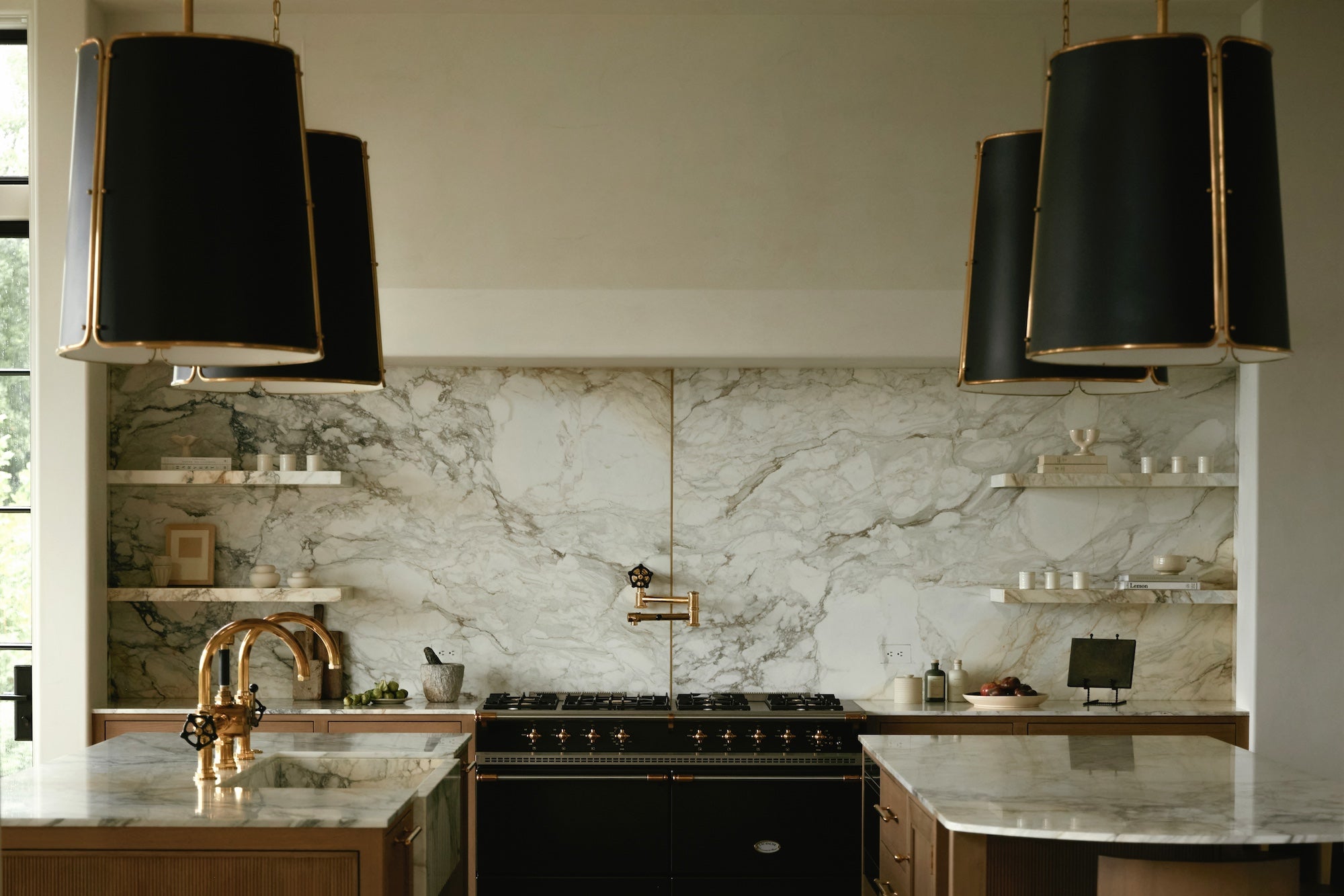 A kitchen with wooden cabinetry, a marble backsplash, and large black and brass pendant lights.
