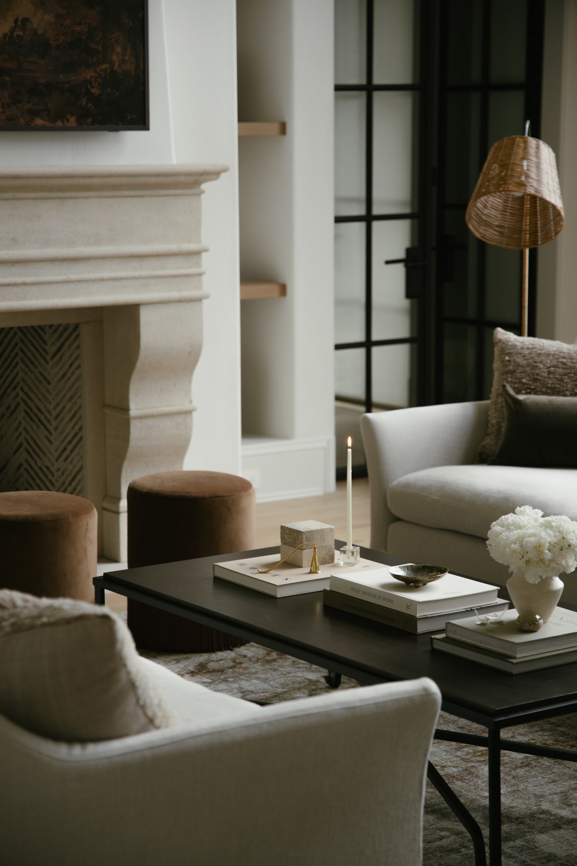 An image of a living room with two light couches, a black coffee table, and two round ottomans.