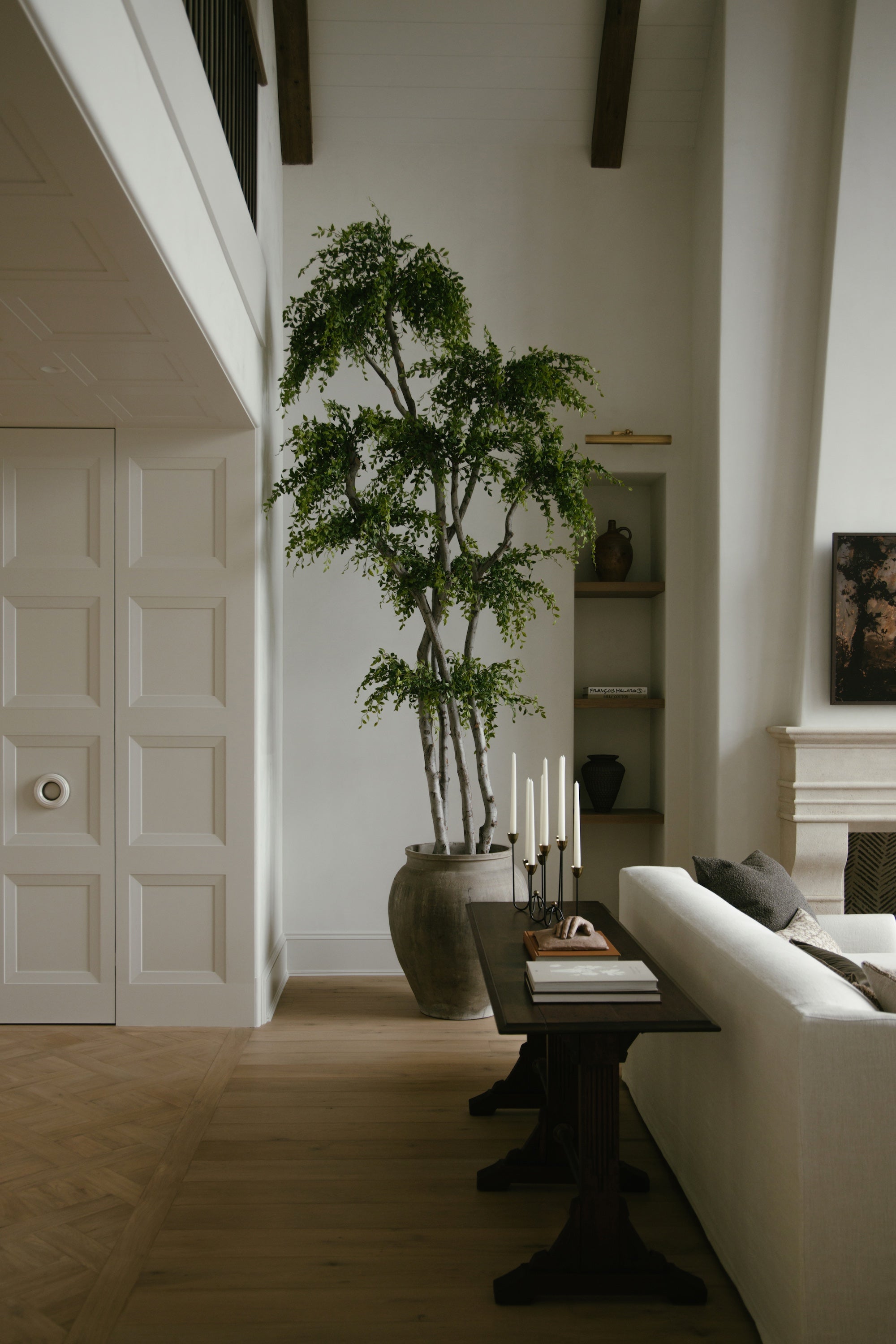 An image of a wooden console table behind a couch, and a potted tree.