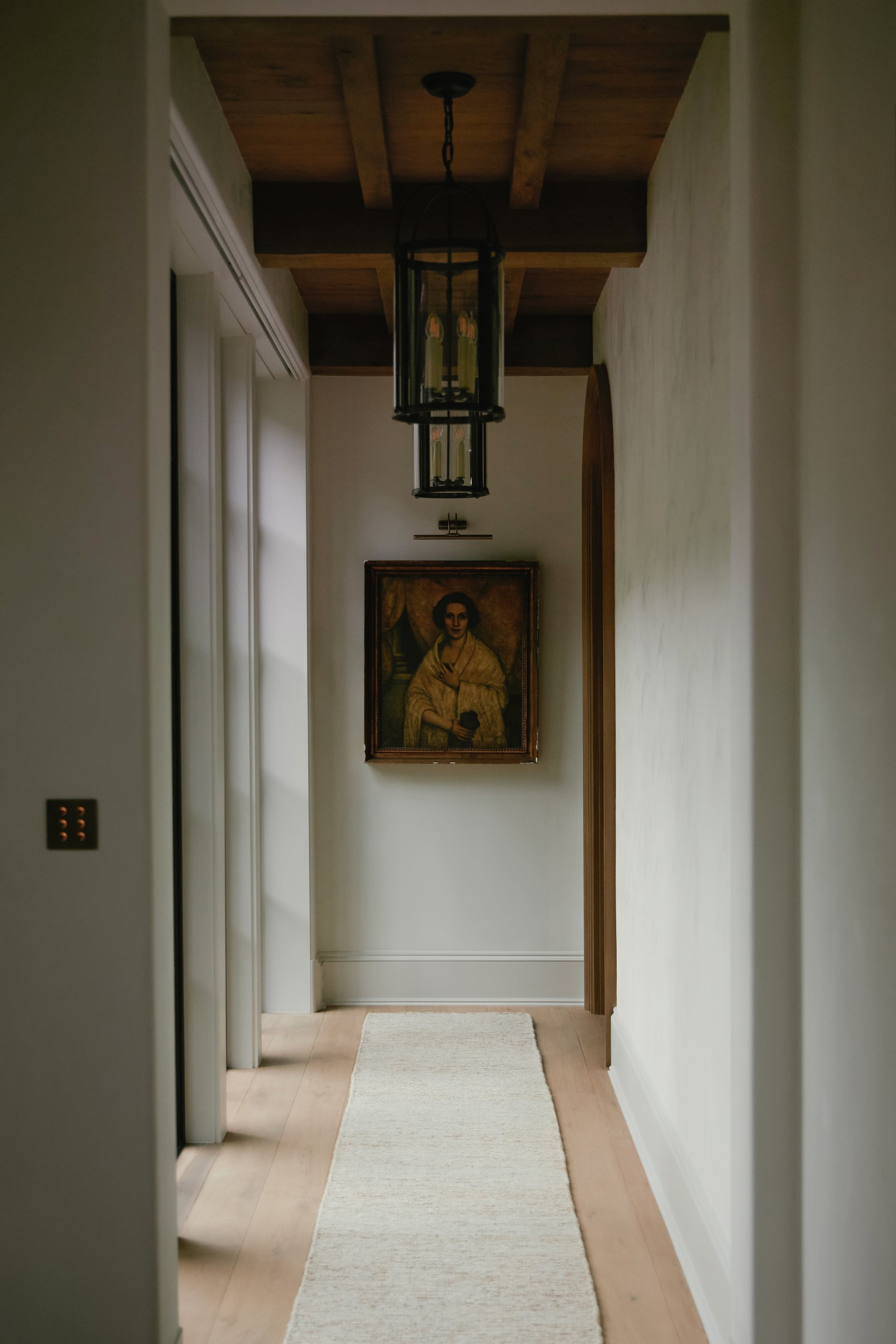 An image looking down a hallway with a wood ceiling and an antique portrait hanging on the wall.