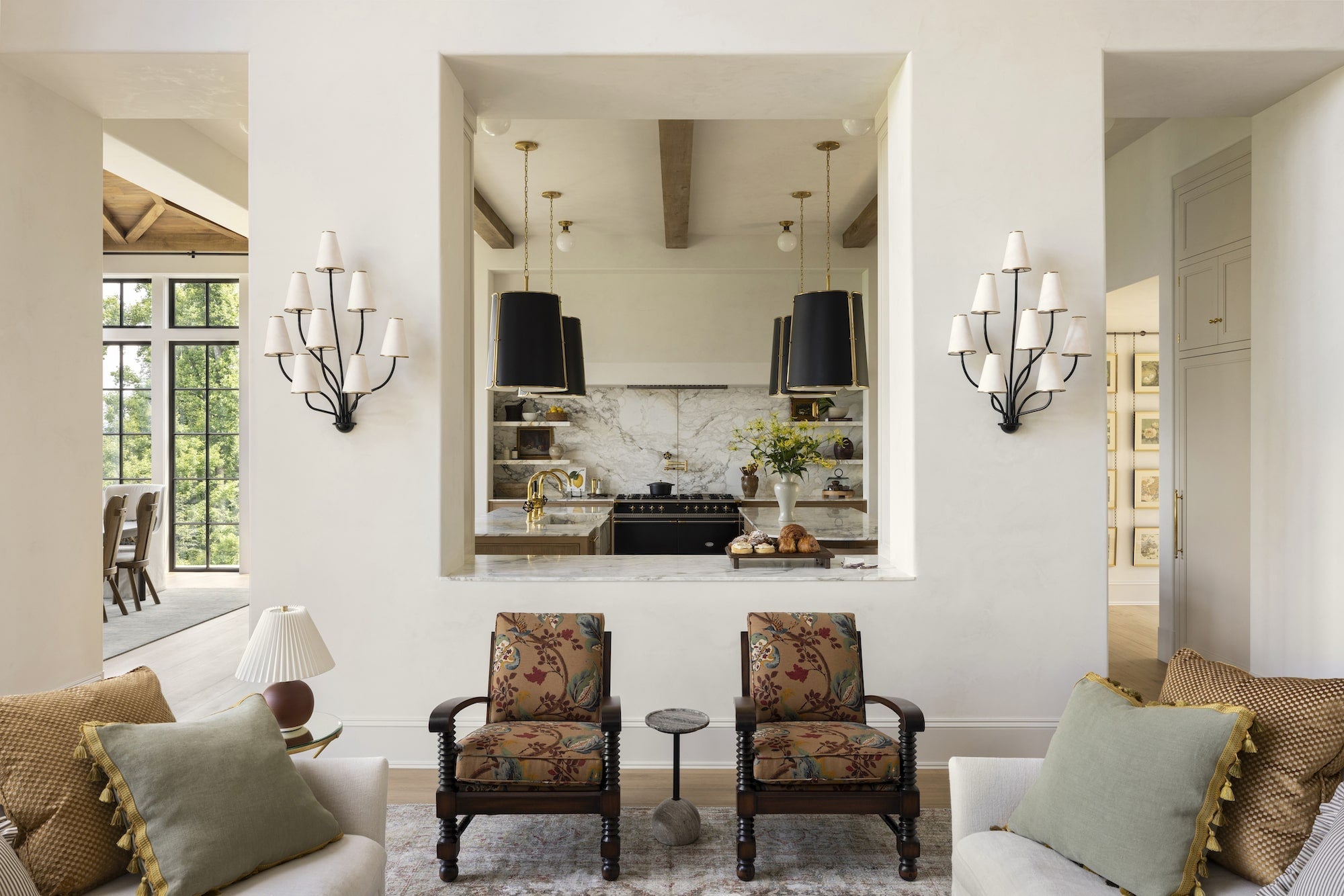 An image of a living room looking into a kitchen. Two upholstered chairs with a wooden frame.