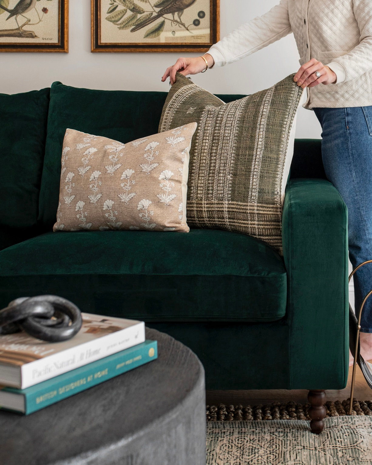 An image of a woman styling pillows on a green couch.