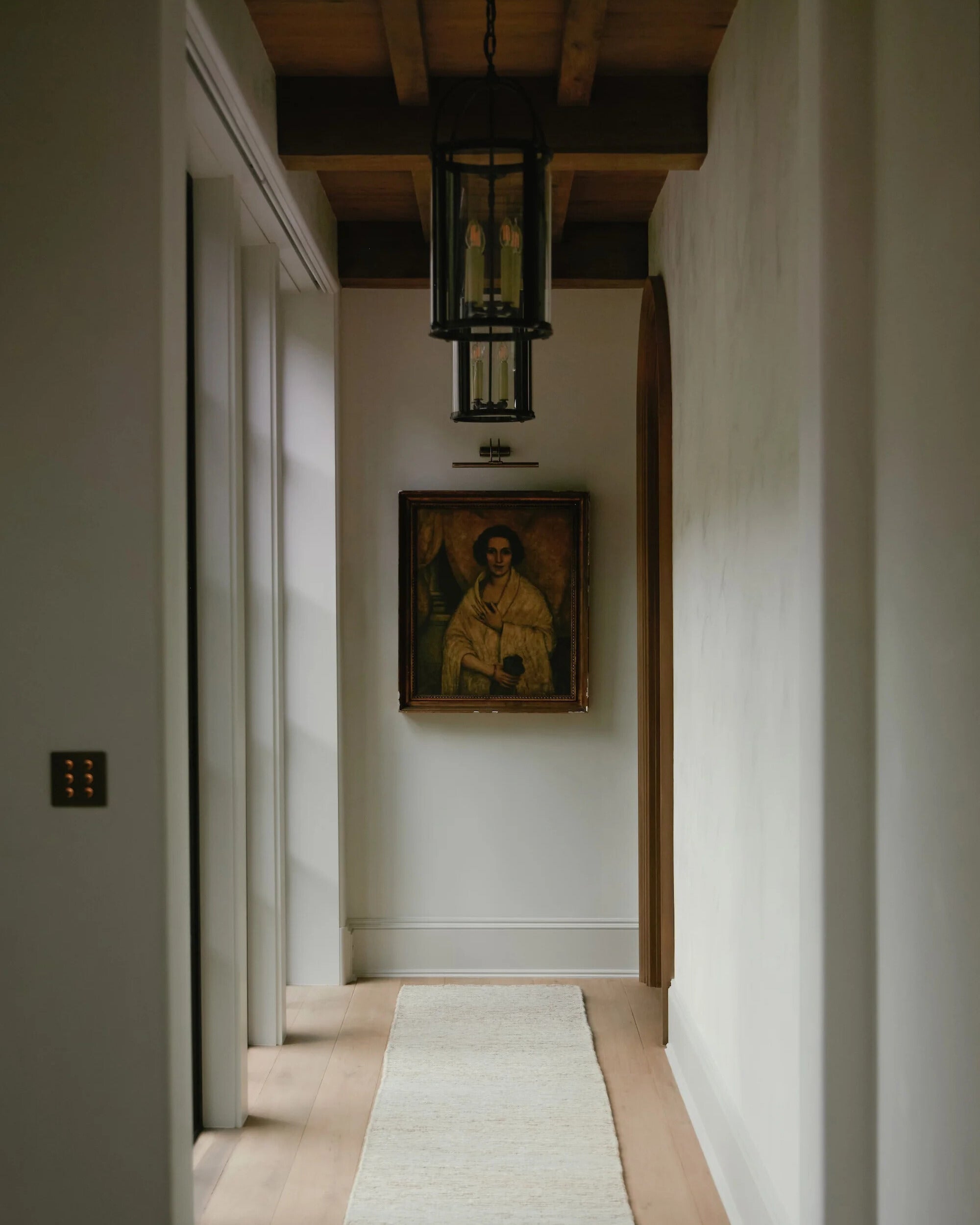 An image of a hallway with a wooden ceiling and antique portrait painting at the end.